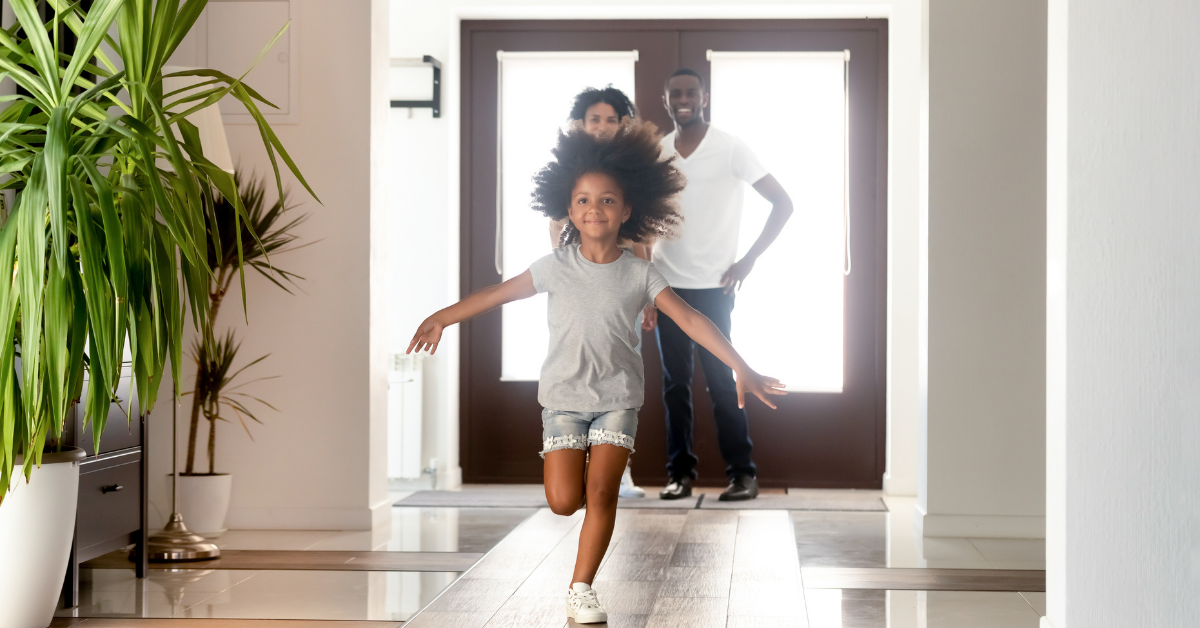 Young girl running into a new home with parents standing by